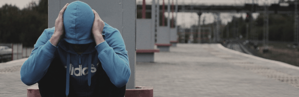 picture of a person in a bluehooded sweatshirt with head in hands and their face not visible