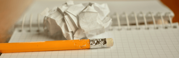 The image shows a pencil and scrunched up paper on top of a note book.